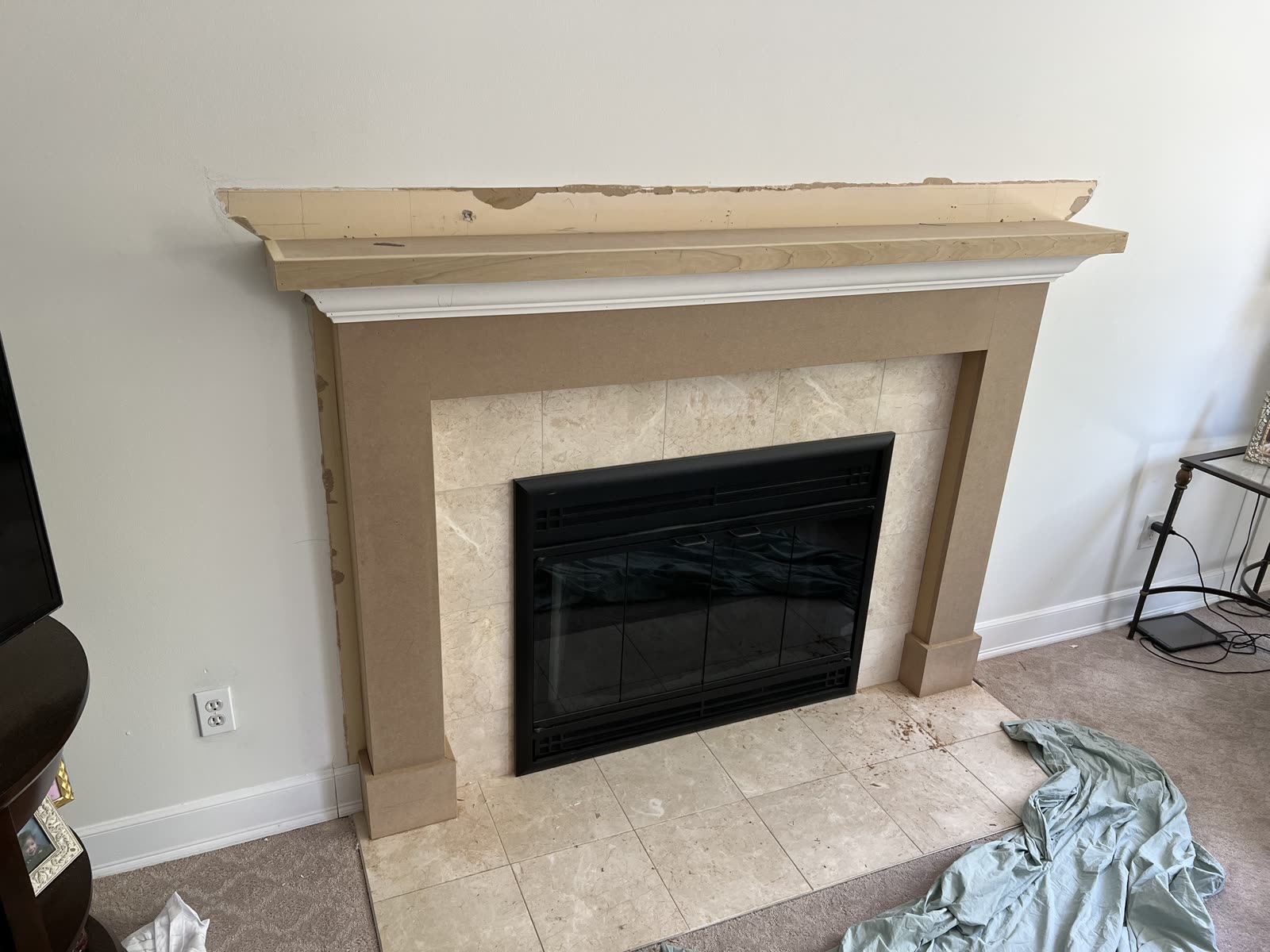 Fireplace mantel mid-build around marble tile: a flat surround with plinth blocks at the floor and a wood shelf over a band of crown.