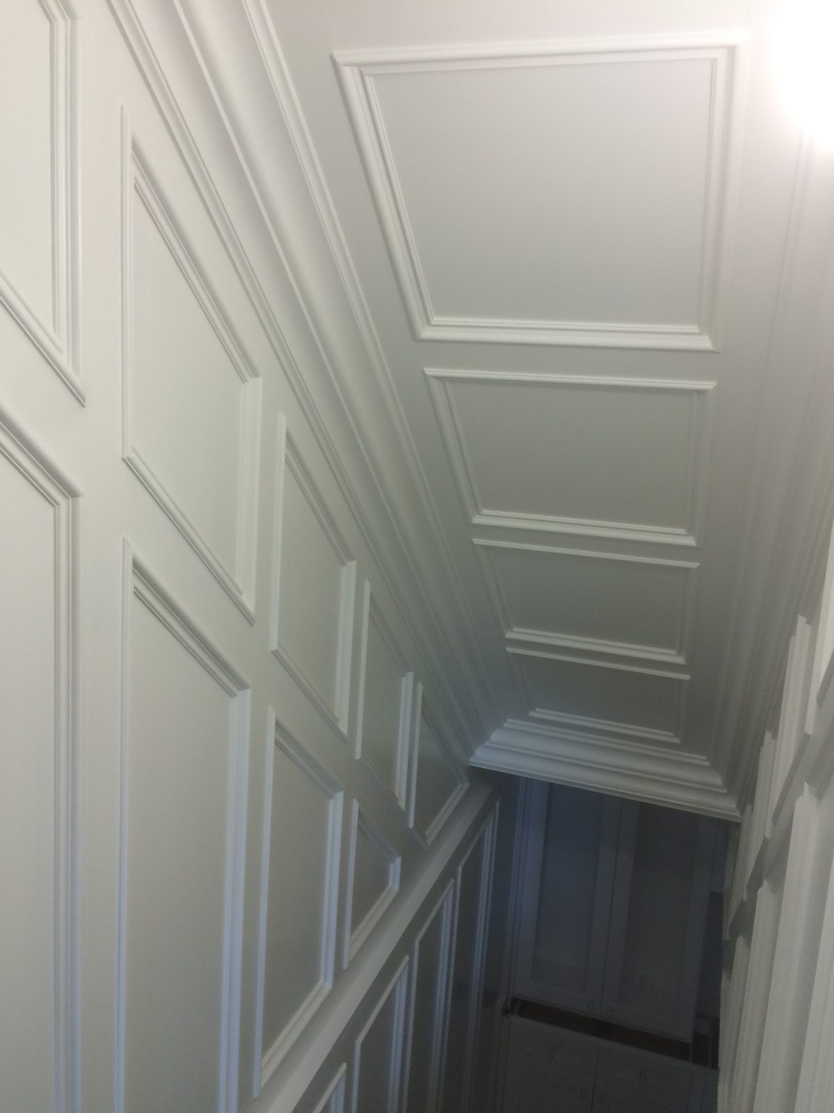 Finished stair hall, painted white: picture-frame molding up the wall along the stairs and across the sloped ceiling above them.