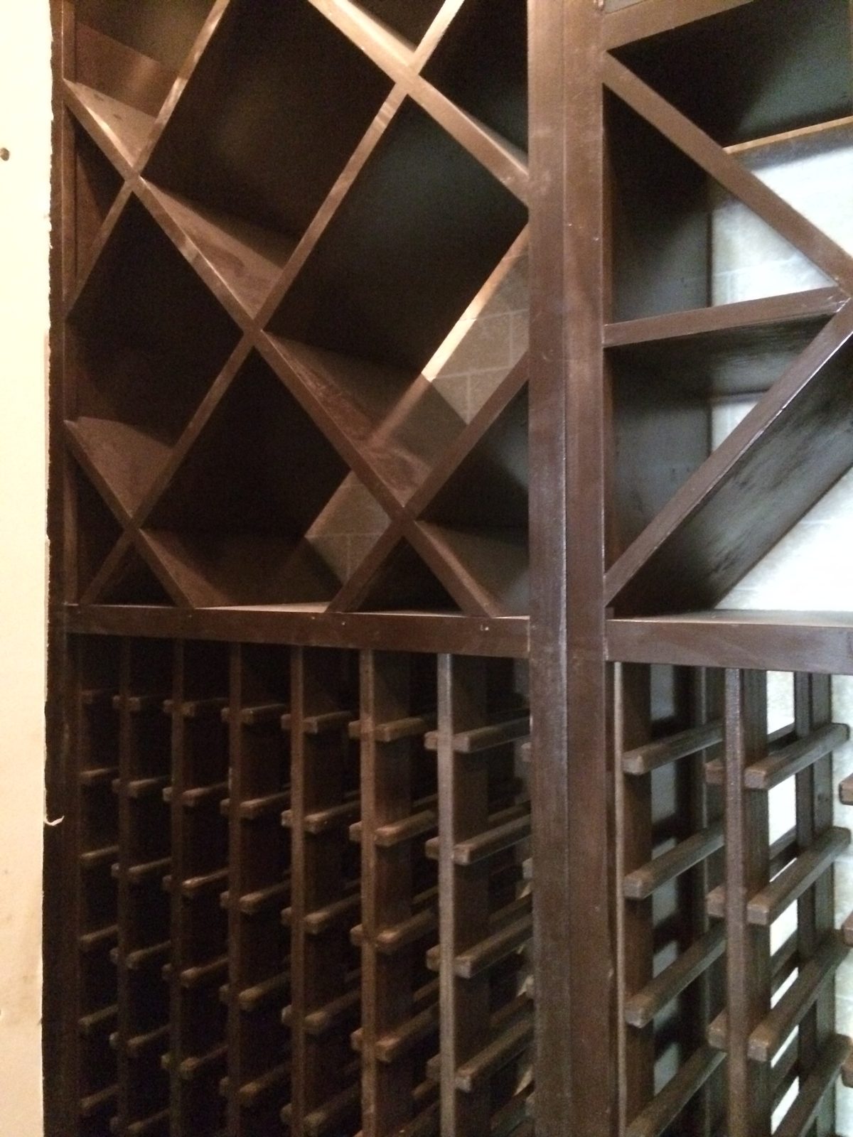 Close view of the stained wine rack: diamond bins over rows of individual bottle racks on wood rails.
