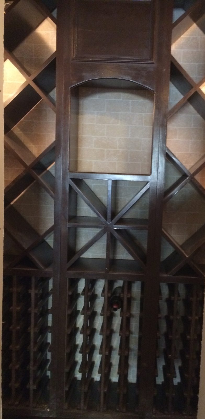 Stained wine rack filling a wall niche: diamond bins at the top, bottle racks below, and an arched opening in the center column.